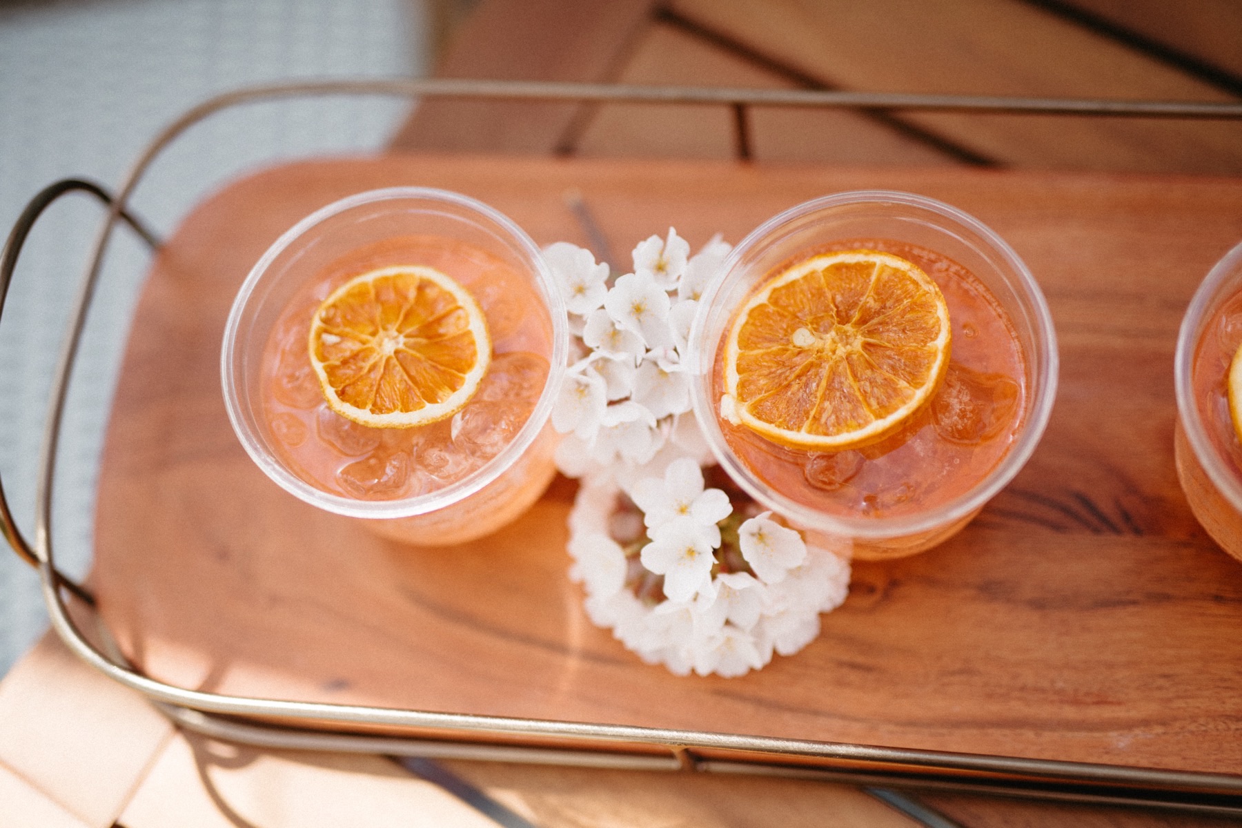 Overhead view of iced pink drinks garnished with dried orange wheels on a wooden tray with white blossoms.